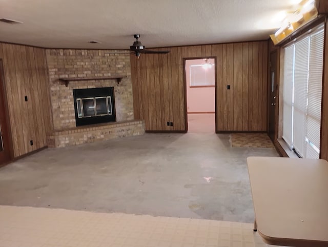 unfurnished living room with ceiling fan, a fireplace, wood walls, concrete floors, and visible vents