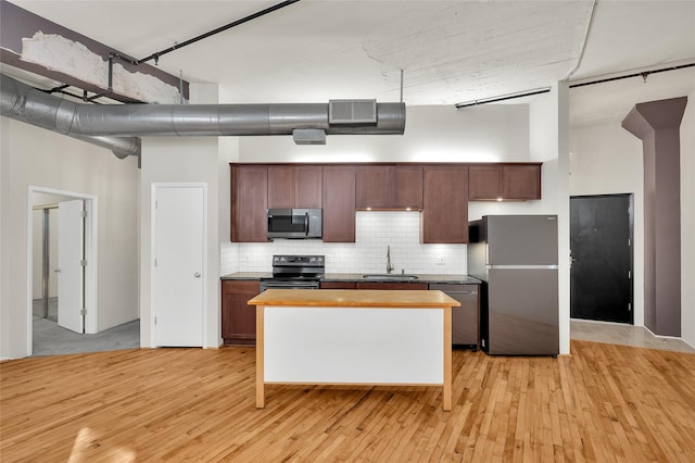 kitchen with a high ceiling, light wood-type flooring, a sink, appliances with stainless steel finishes, and backsplash