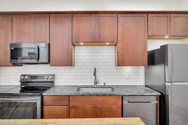 kitchen with backsplash, appliances with stainless steel finishes, a sink, and dark stone counters