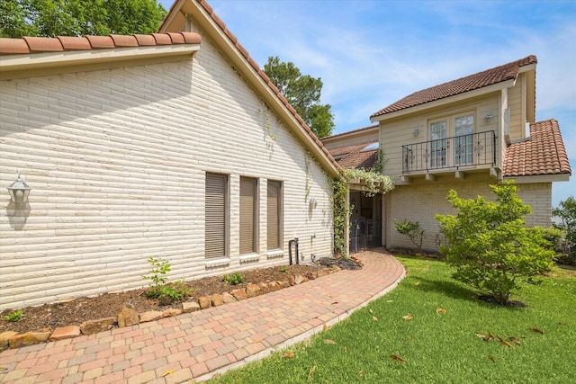 back of property featuring french doors, a yard, brick siding, and a balcony