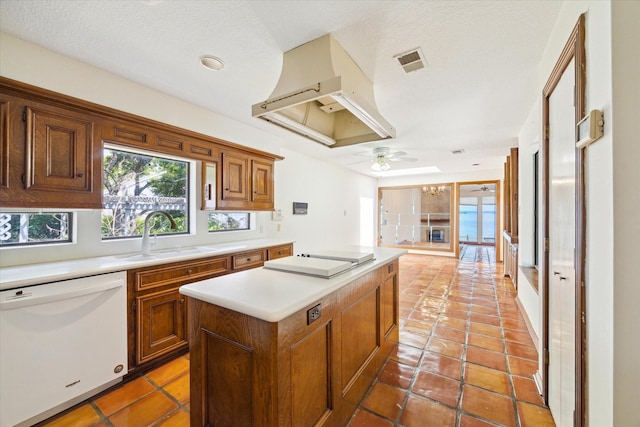 kitchen featuring a sink, dishwasher, premium range hood, cooktop, and visible vents