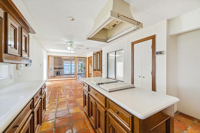 kitchen featuring brown cabinetry, a kitchen island, ceiling fan, light countertops, and a sink