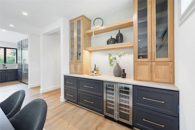 bar with beverage cooler, baseboards, a bar, and light wood-style floors