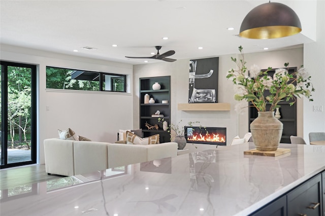 living area with a glass covered fireplace, built in shelves, recessed lighting, a ceiling fan, and visible vents
