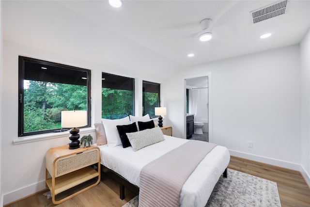 bedroom featuring visible vents, baseboards, ensuite bathroom, and wood finished floors