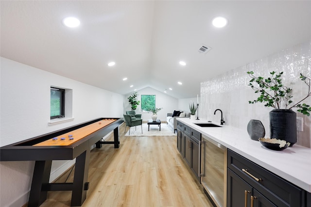 interior space featuring wine cooler, light wood-style floors, light countertops, a sink, and vaulted ceiling