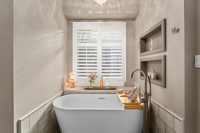 full bath featuring a freestanding tub and a textured wall