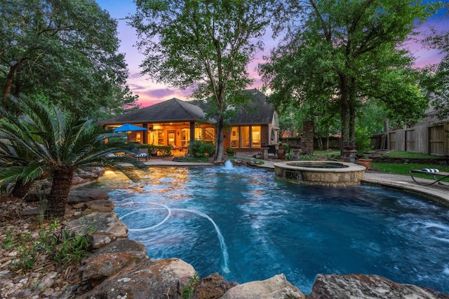 pool at dusk featuring a patio, a pool with connected hot tub, and fence