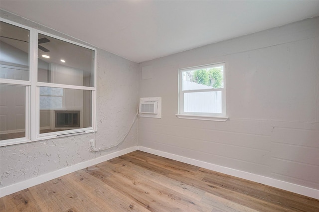 empty room featuring baseboards, a wall mounted AC, and wood finished floors