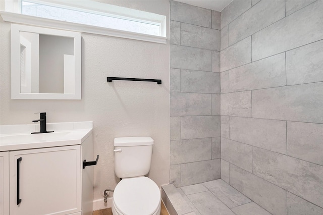 bathroom with vanity, toilet, and tiled shower