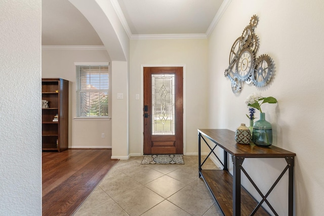 entrance foyer featuring crown molding, arched walkways, baseboards, and light tile patterned floors