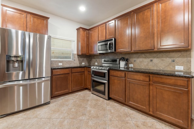 kitchen with appliances with stainless steel finishes, tasteful backsplash, brown cabinetry, and dark stone countertops