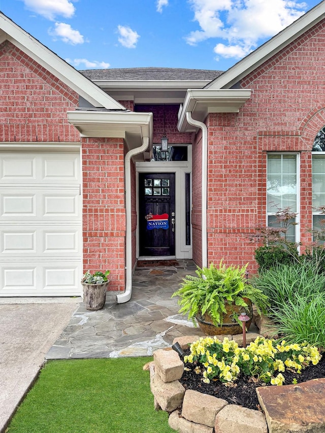 view of exterior entry featuring brick siding, a garage, and driveway