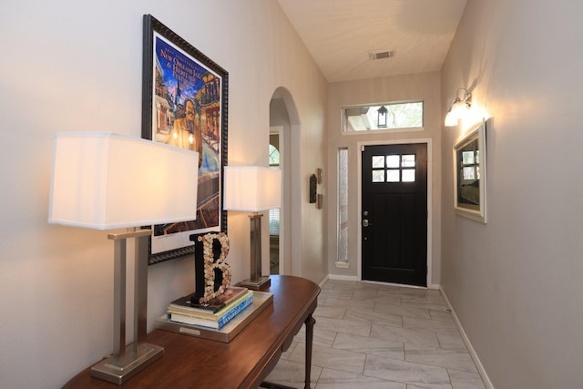 foyer featuring arched walkways, light marble finish flooring, and baseboards