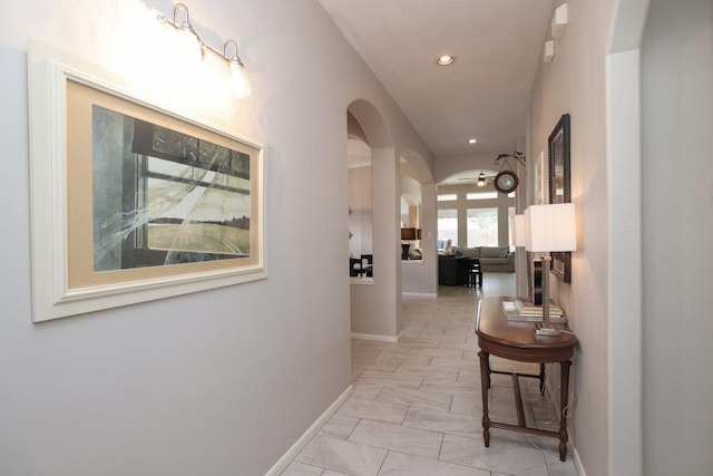 hall with arched walkways, baseboards, recessed lighting, and light marble finish floors