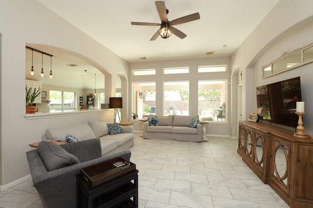 living room featuring a ceiling fan, light marble finish flooring, arched walkways, and baseboards