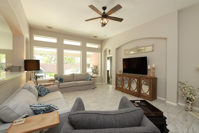 living area with a ceiling fan, arched walkways, light marble finish flooring, and baseboards