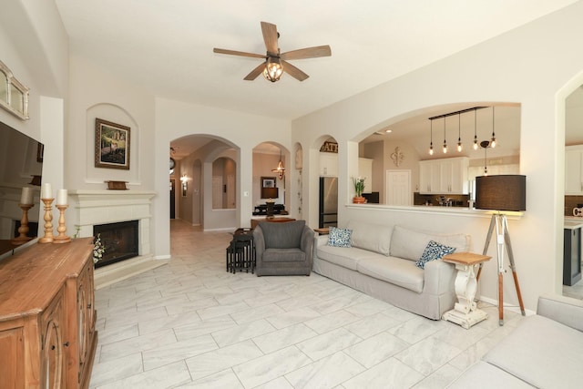 living area with ceiling fan, a fireplace with raised hearth, and arched walkways
