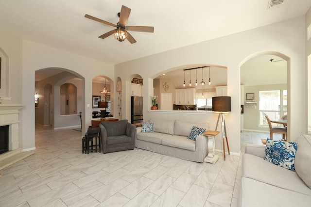 living area featuring ceiling fan, a glass covered fireplace, and light marble finish floors