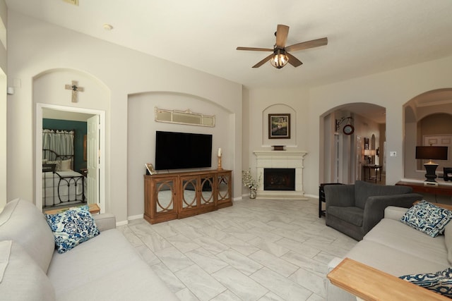 living room with a ceiling fan, arched walkways, a fireplace with raised hearth, and light marble finish floors