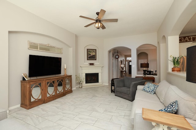 living room with a ceiling fan, arched walkways, a fireplace with raised hearth, and light marble finish floors
