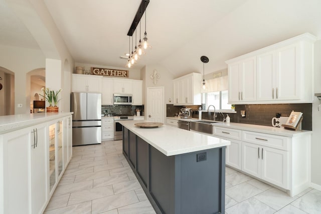kitchen featuring stainless steel appliances, a sink, a kitchen island, light marble finish floors, and arched walkways