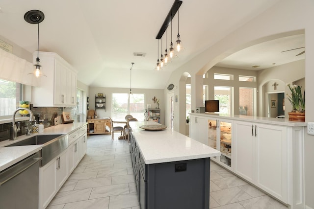 kitchen featuring stainless steel dishwasher, a sink, light marble finish floors, a kitchen island, and arched walkways