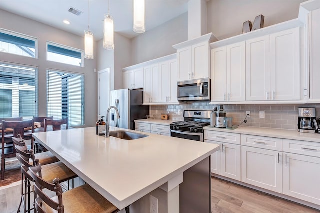kitchen with a kitchen breakfast bar, backsplash, a sink, stainless steel appliances, and an island with sink