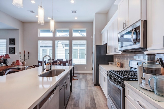 kitchen with a sink, light countertops, stainless steel appliances, white cabinetry, and pendant lighting