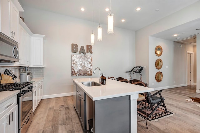 kitchen with a breakfast bar area, appliances with stainless steel finishes, light wood-type flooring, a sink, and an island with sink