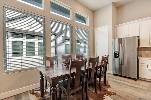 dining space featuring light wood-type flooring, baseboards, and a towering ceiling