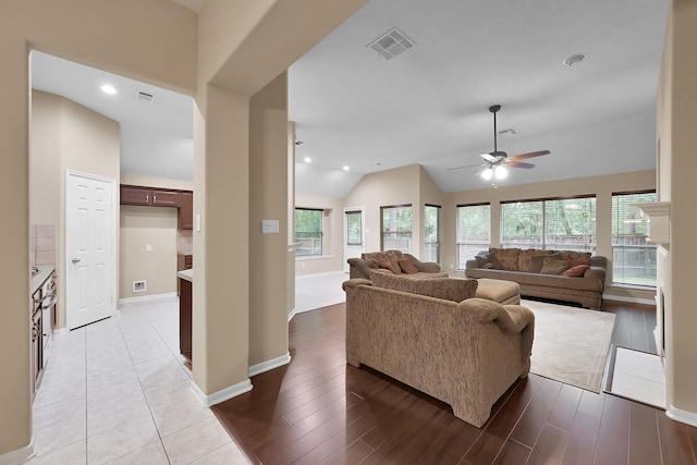 living area featuring a ceiling fan, visible vents, baseboards, lofted ceiling, and light wood-style flooring