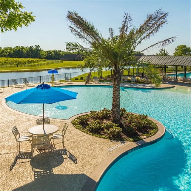 pool with a water view, a patio area, and fence