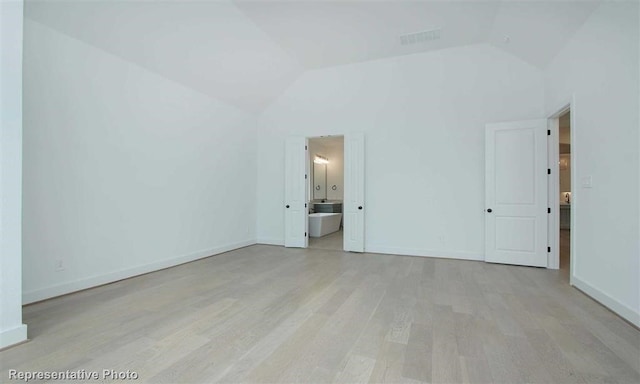 unfurnished bedroom with visible vents, vaulted ceiling, baseboards, ensuite bath, and light wood-style flooring