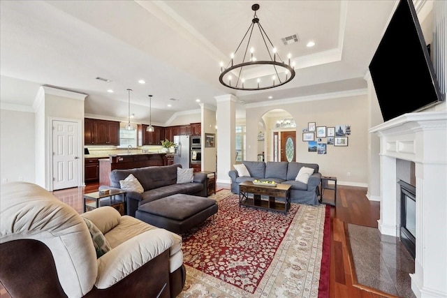living area with arched walkways, wood finished floors, a raised ceiling, a chandelier, and recessed lighting