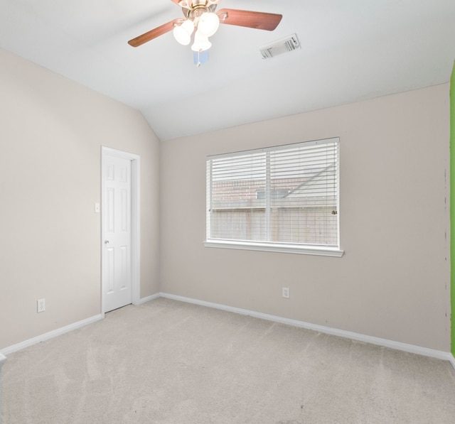empty room featuring light colored carpet, a ceiling fan, baseboards, lofted ceiling, and visible vents