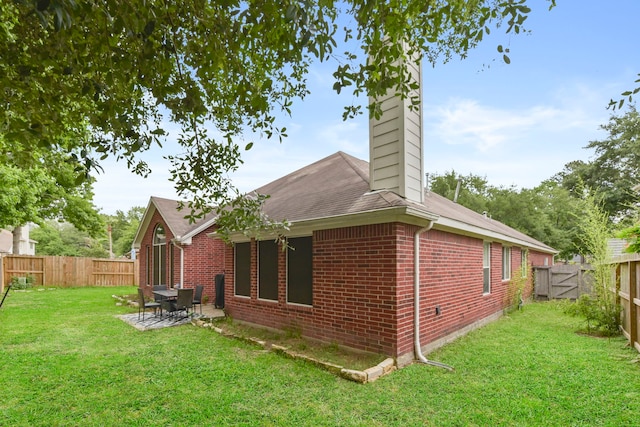 rear view of property with a fenced backyard, a chimney, a lawn, and brick siding