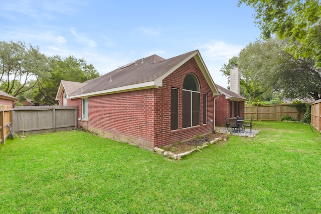 view of side of property featuring a patio, a fenced backyard, a chimney, brick siding, and a yard