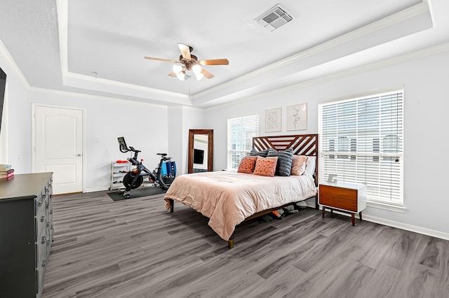 bedroom featuring visible vents, wood finished floors, a raised ceiling, baseboards, and ornamental molding