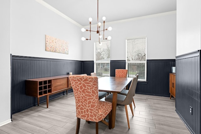 dining area with a wainscoted wall, ornamental molding, and light wood finished floors