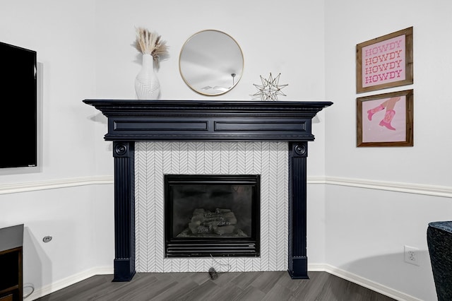 room details featuring baseboards, a tiled fireplace, and wood finished floors