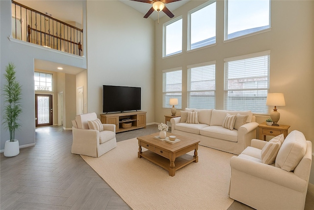 living area with a ceiling fan, baseboards, and a towering ceiling