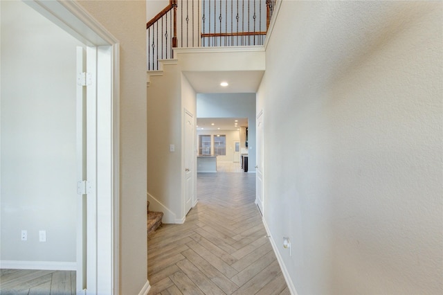 corridor with stairway, a high ceiling, and baseboards
