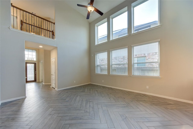 empty room featuring ceiling fan, a high ceiling, baseboards, and a wealth of natural light