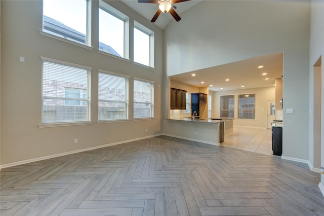 unfurnished living room featuring a high ceiling, baseboards, ceiling fan, and a sink