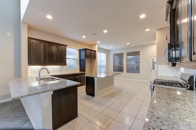 kitchen with dark brown cabinets, a sink, gas range, decorative backsplash, and light stone counters
