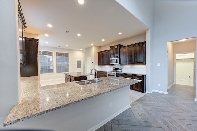 kitchen with a sink, baseboards, backsplash, a kitchen island, and appliances with stainless steel finishes