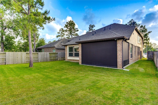 back of property featuring a fenced backyard, a shingled roof, brick siding, and a lawn