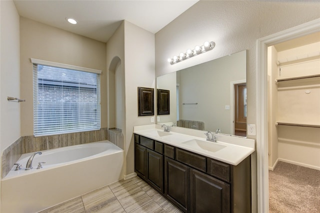 bathroom featuring a sink, double vanity, a spacious closet, and a bath