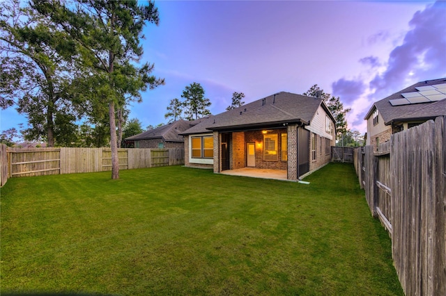 back of house at dusk featuring a yard, a patio, brick siding, and a fenced backyard